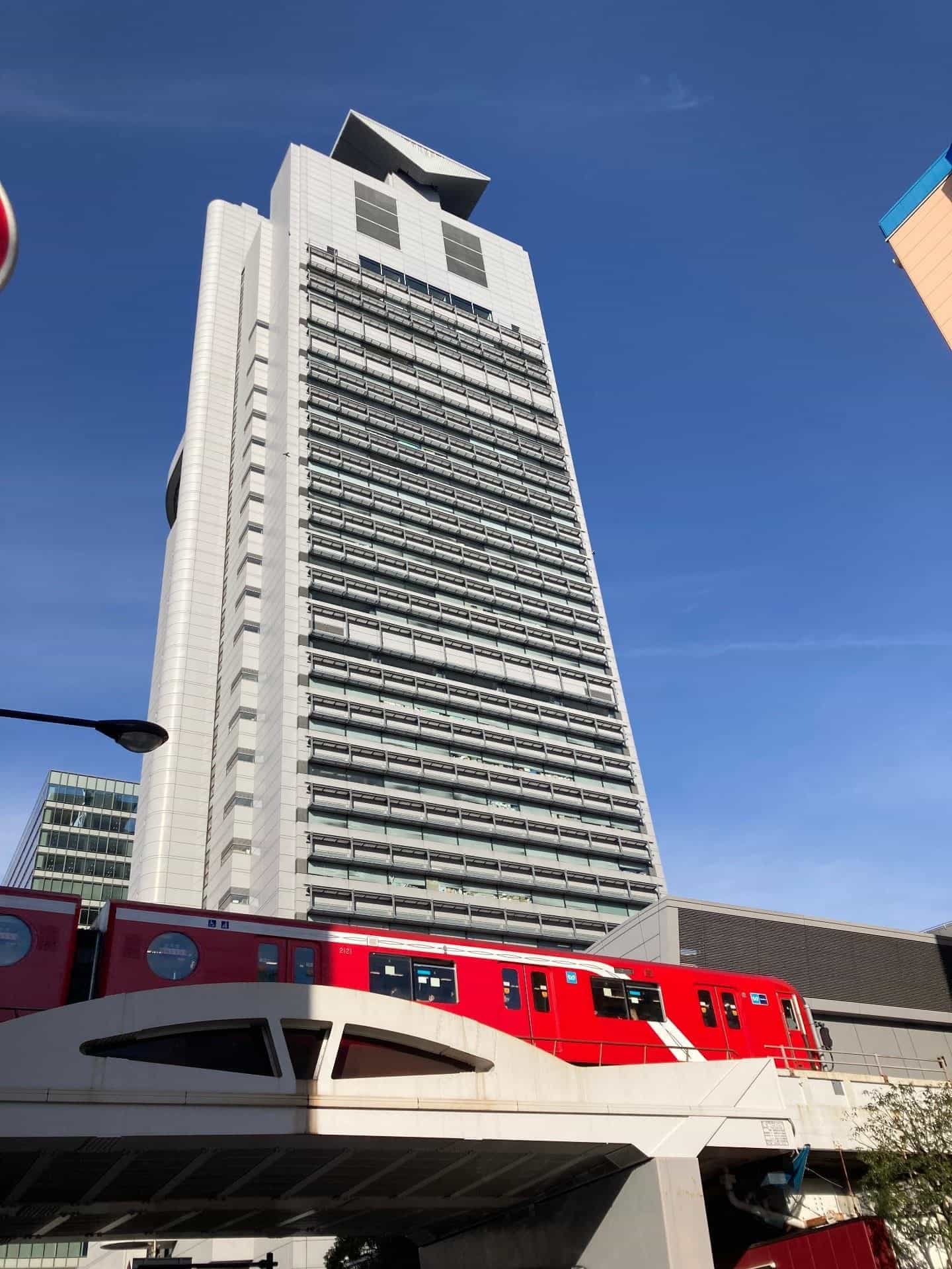Torre del Bunkyo Civic Center vista dal basso, con un treno rosso della linea Marunouchi che passa davanti all’edificio