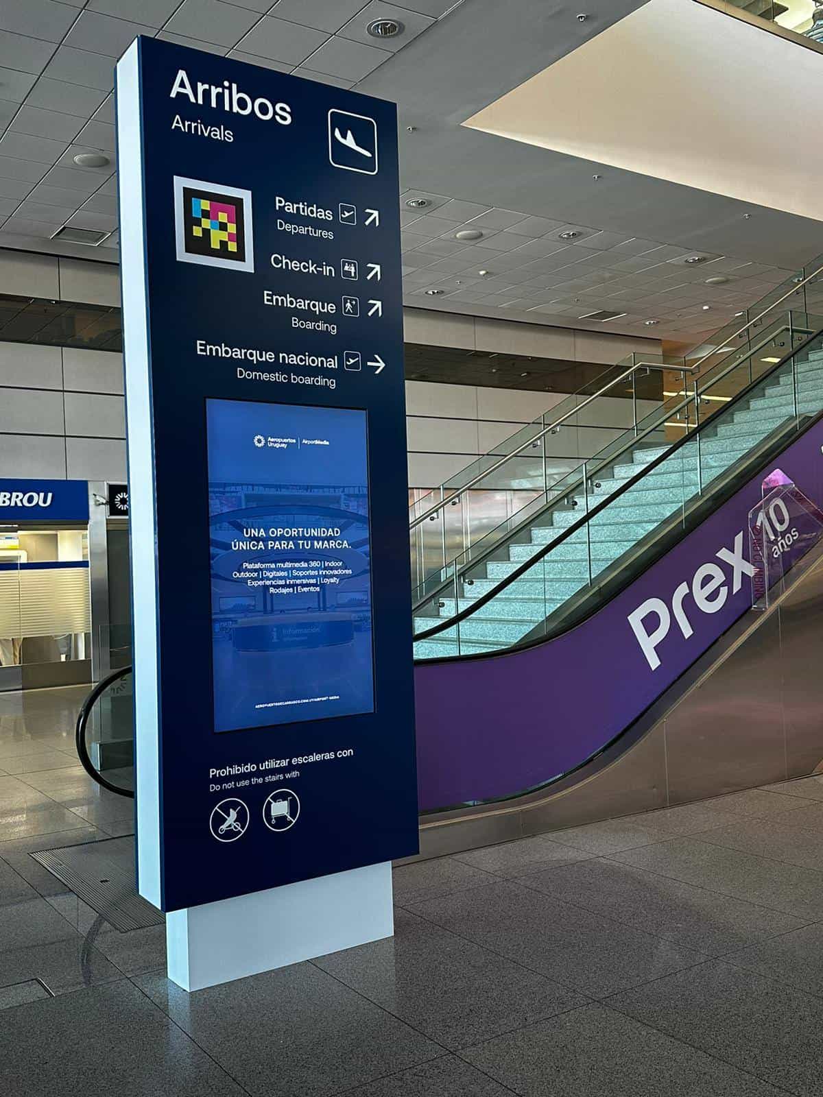 Flight information display (FIDS) at Gate 2 of Carrasco Airport showing JetSmart's flight to Rio with an active NaviLens marker that reads gate, time and destination by voice
