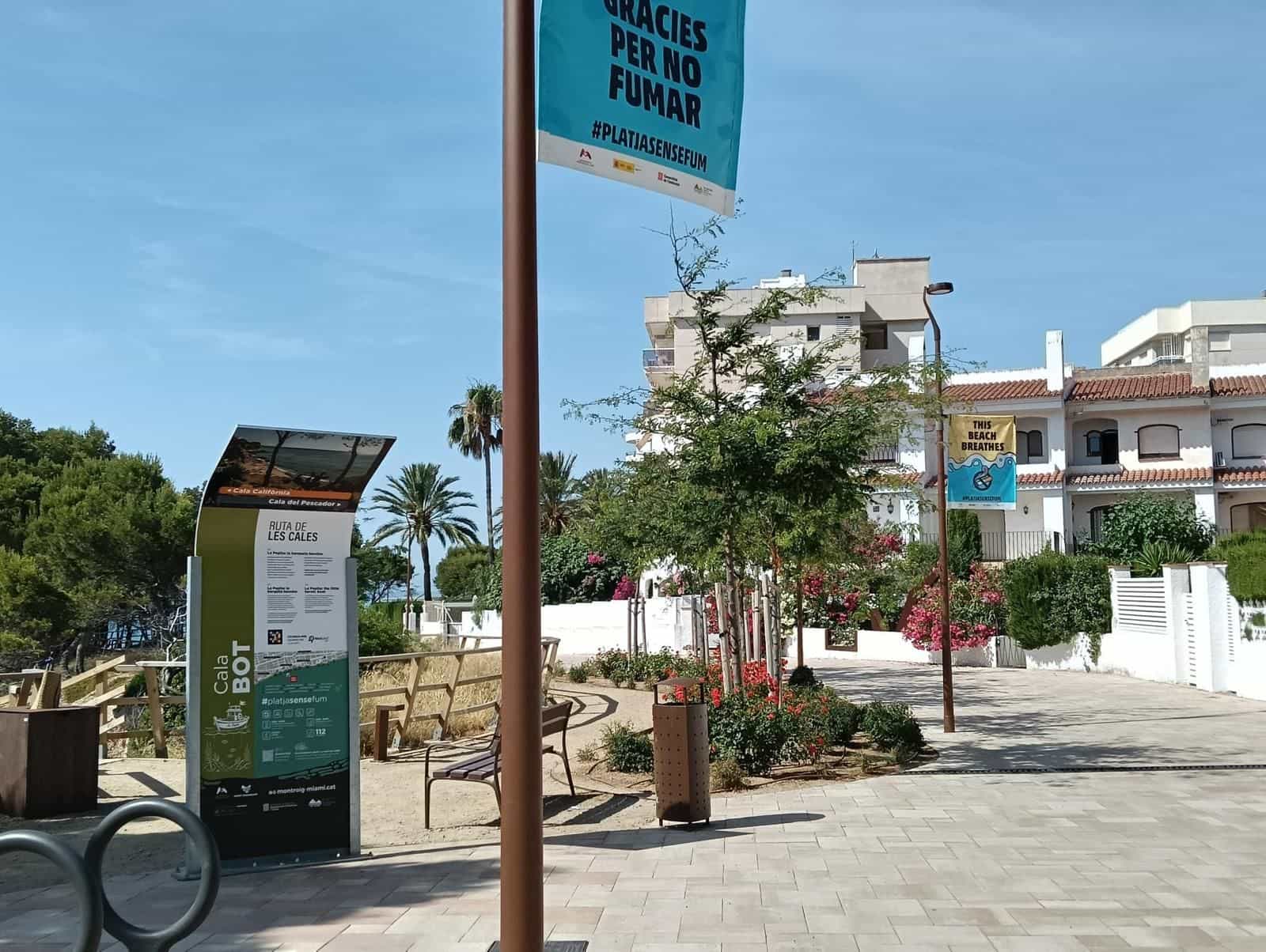 Totem der Cala Bot auf einem Platz der Promenade, daneben ein Banner «Gràcies per no fumar» der Kampagne #platjasensefum