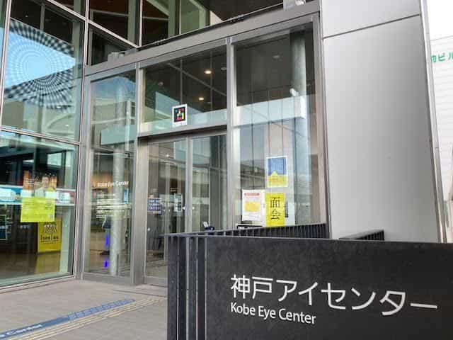 神戸アイセンター入口の別アングル。自動扉の上のNaviLensタグ、ガラスに貼られたisee!キャンペーンの掲示、来館者向け日本語案内が見える