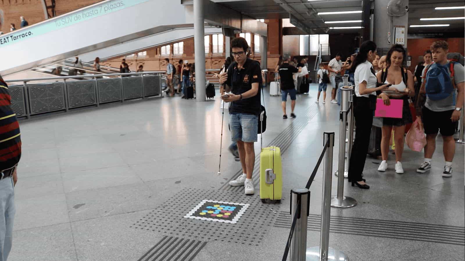 Un utente con bastone bianco usa un codice NaviLens a terra accanto alle scale ad Atocha