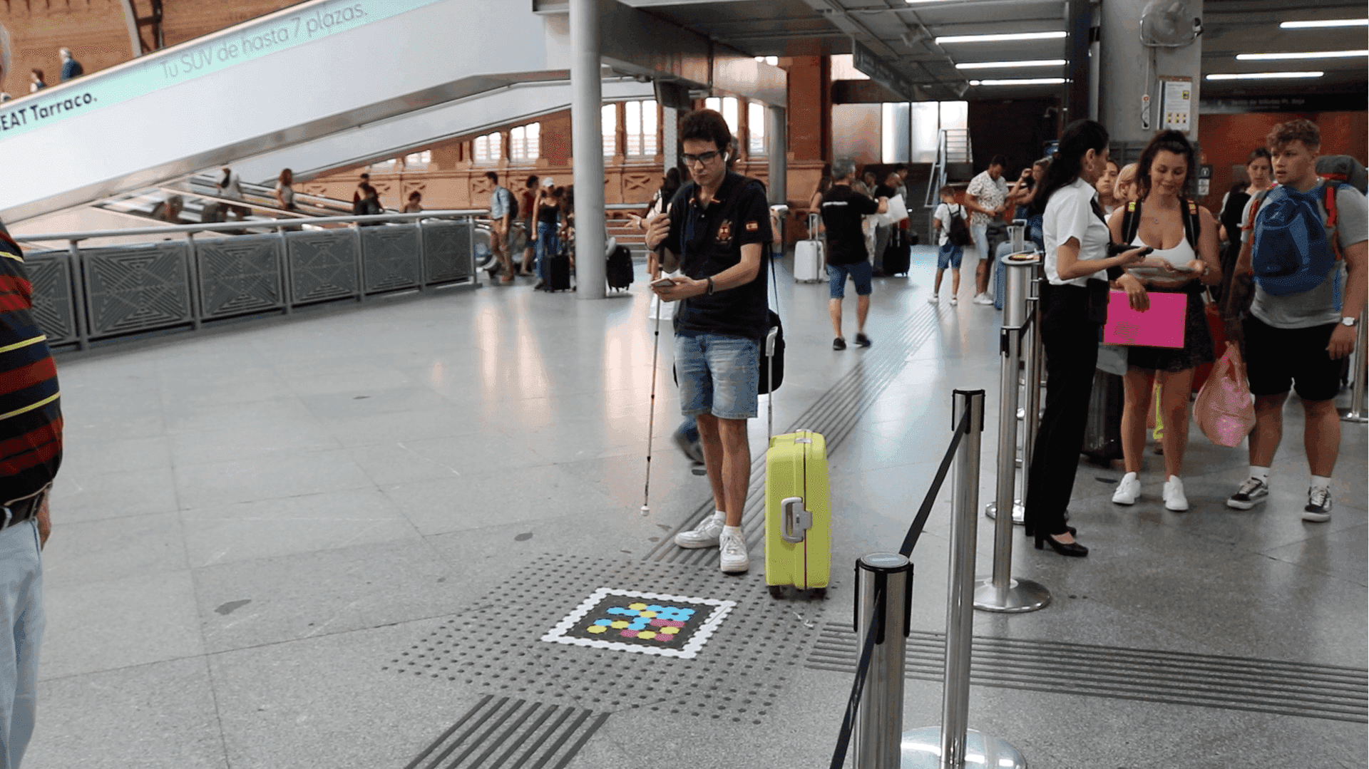 Usuario con bastón blanco usando un código NaviLens en suelo junto a escaleras en Atocha
