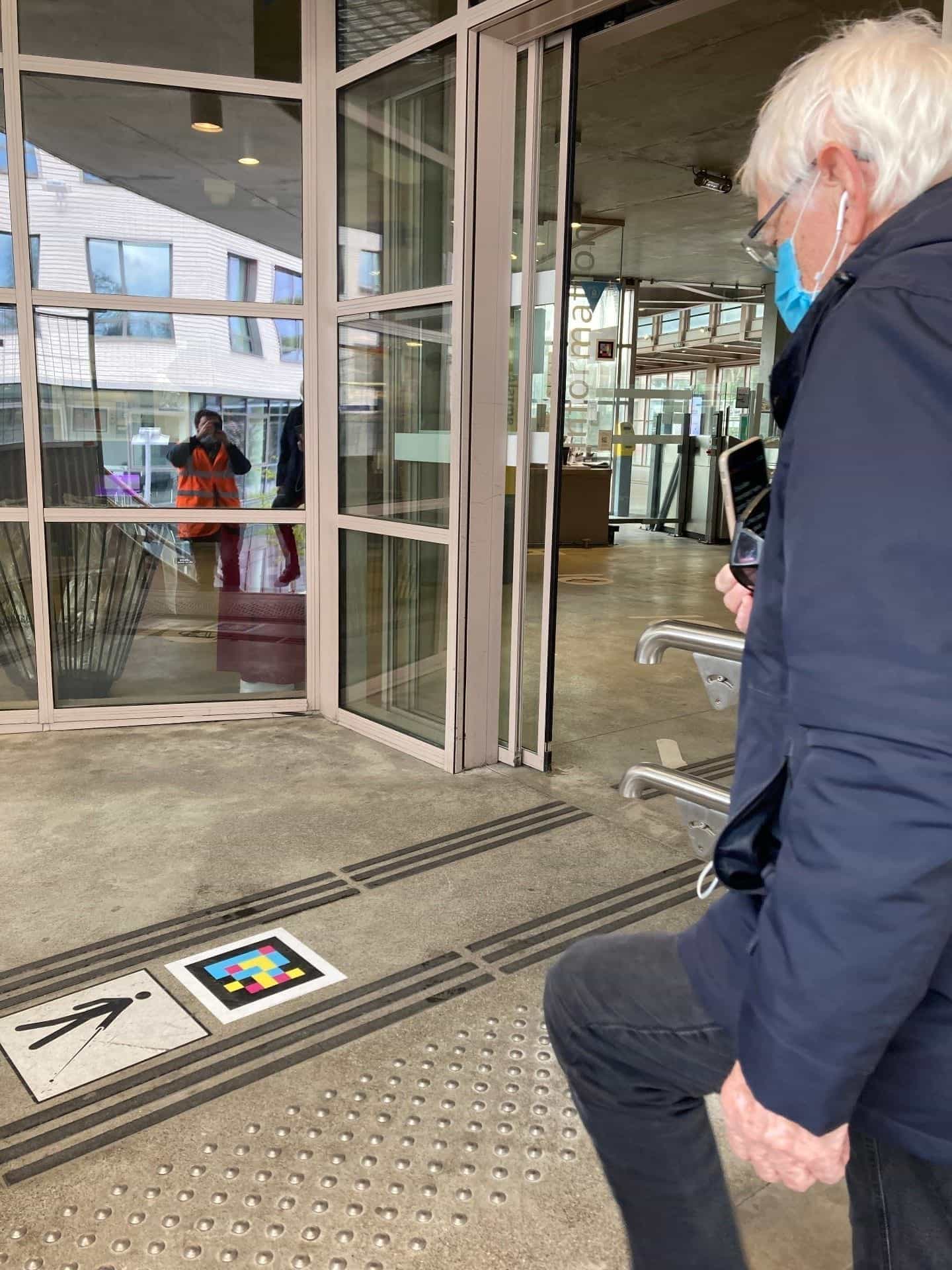 Older man scanning a NaviLens code on the floor by the glass Information door.
