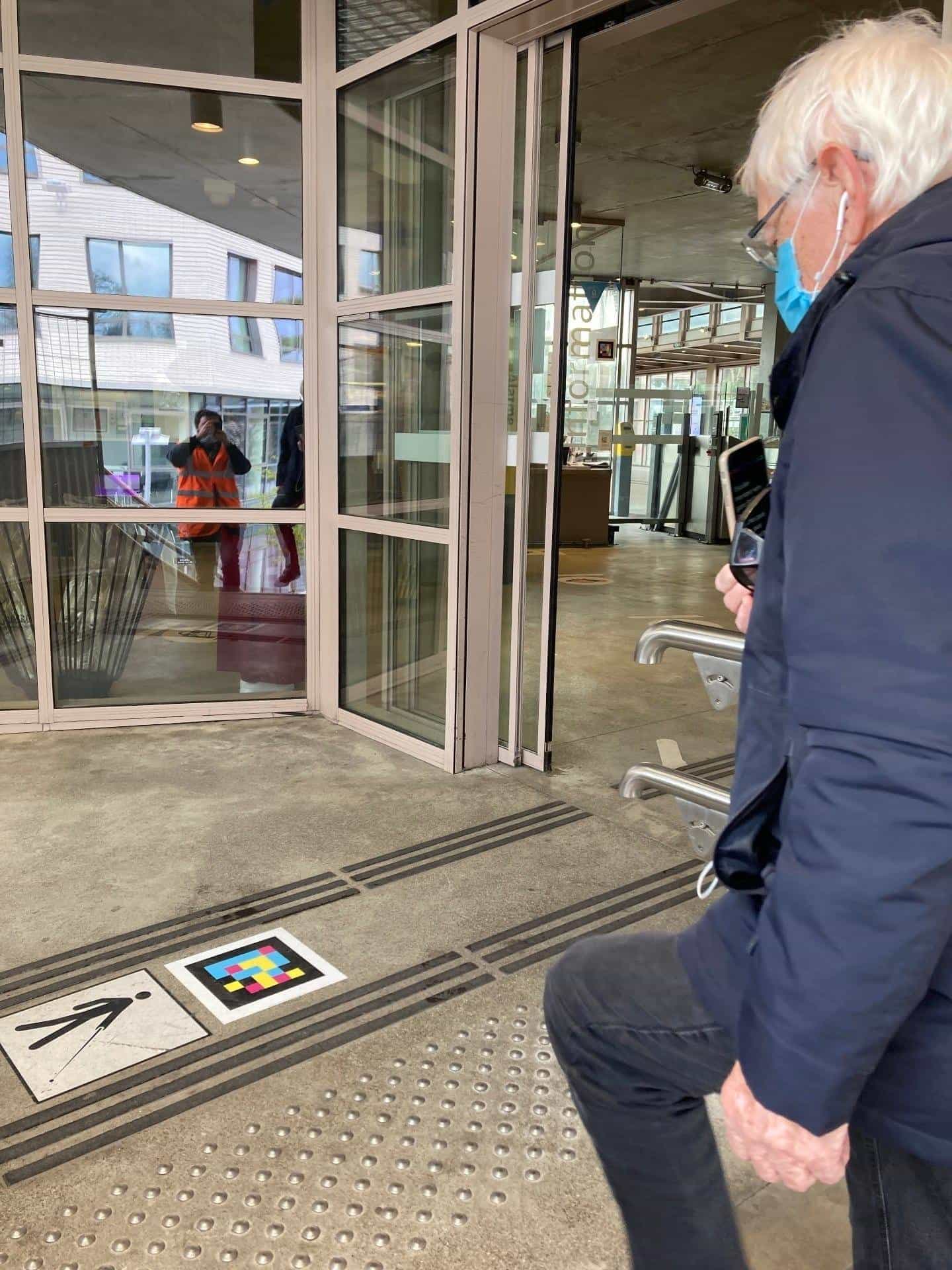 Older man scanning a NaviLens code on the floor by the glass Information door.