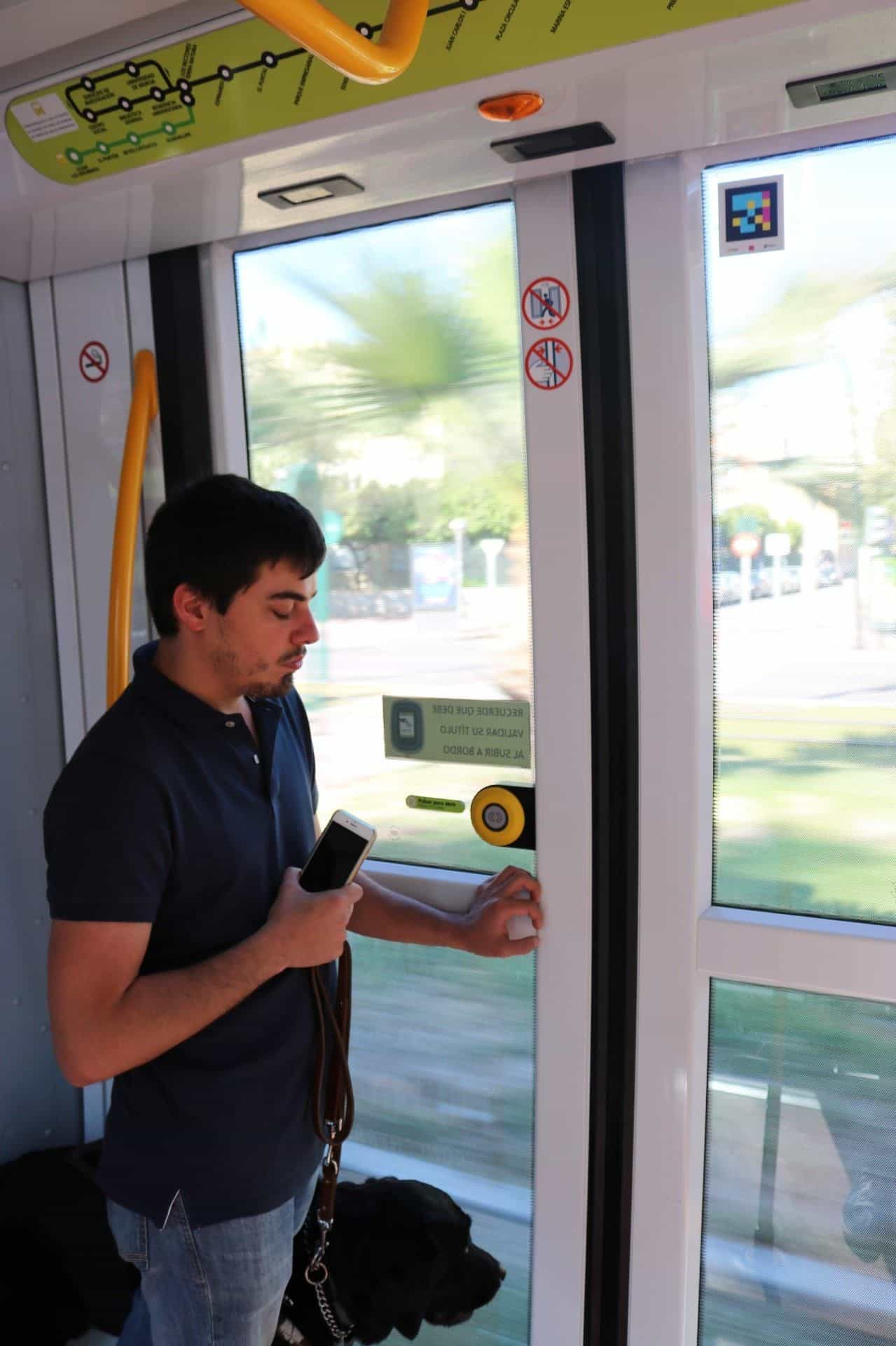 Persona che inquadra un codice NaviLens collocato in cima a una pensilina del Tranvía de Murcia, con lo schermo LED dei prossimi arrivi in fondo