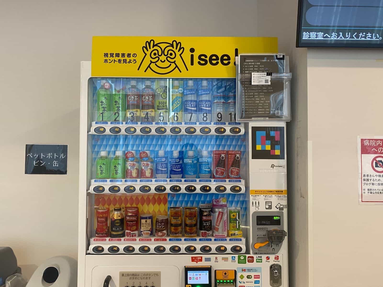 isee!自販機:黄色の「視覚障害者のホントを見よう / i see!」ポスターと、右側面の大型NaviLens GOタグ。視覚障害のある方が白杖からでもブランド・フレーバー・価格・各ボタン位置を音声で聞ける