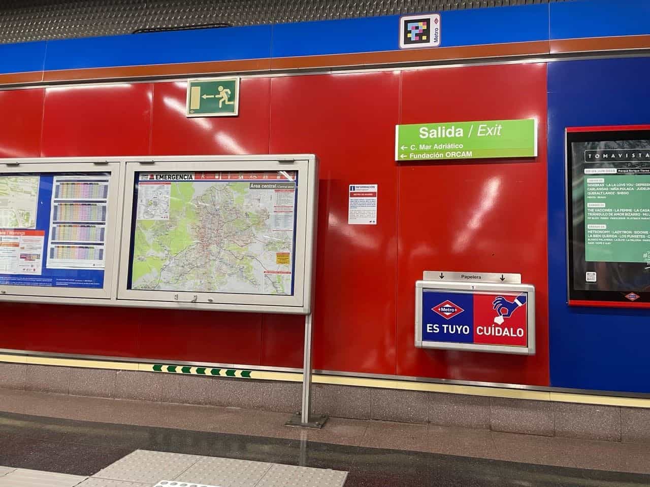 Verteilerebene Mar de Cristal: an der oberen Kante, über dem blau-rosa Streifen der Linie 8, ein gerahmter NaviLens-Code neben der roten Metro-Raute; darunter grünes Panel „Ausgang/Exit – C. Mar Adriático · Fundación ORCAM“, Notfall-Piktogramm, Metro-Plan und rechts ein Werbe-MUPI