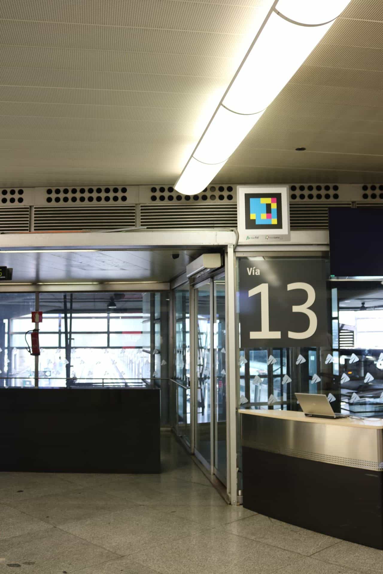 Access to platform 13 at Atocha: above the lintel of the automatic doors, a colorful square NaviLens code with the ‘Adif' and ‘NaviLens GO' logos; next to it, a dark sign with a large number 13 marks the platform.