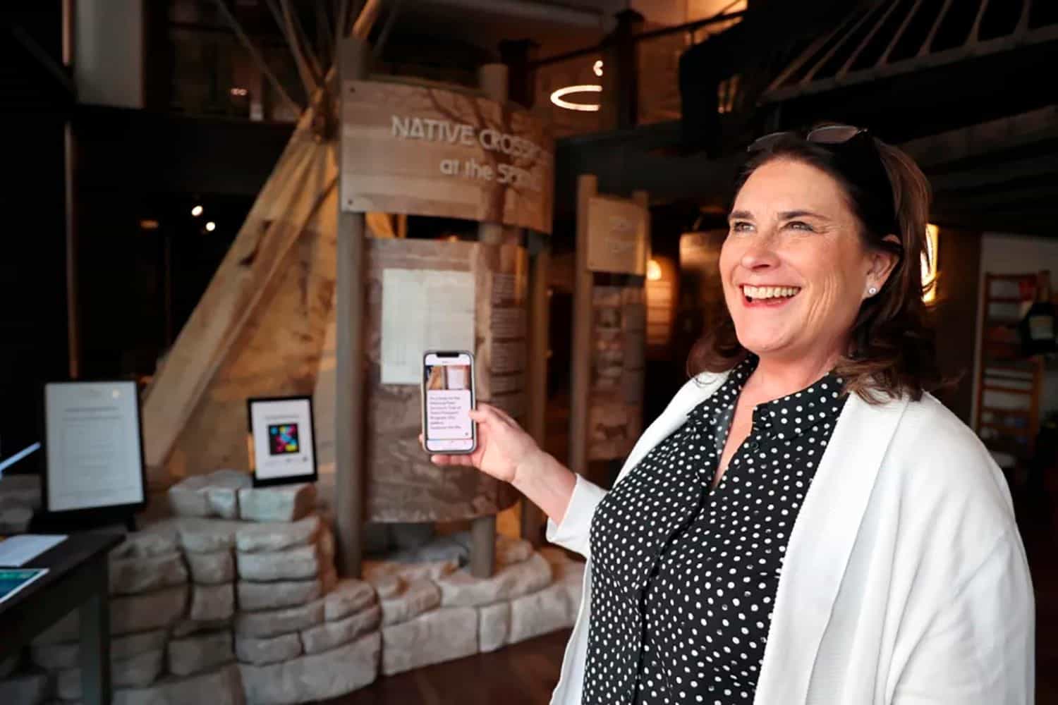 Smiling visitor beside the Native Crossroads tipi exhibit at the History Museum on the Square, with a NaviLens code on the panel