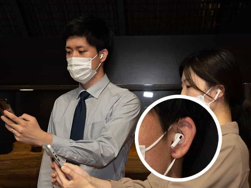 展示室でイヤホンを付けて音声ガイドを聞く2人の来館者。イヤホンのクローズアップ付き