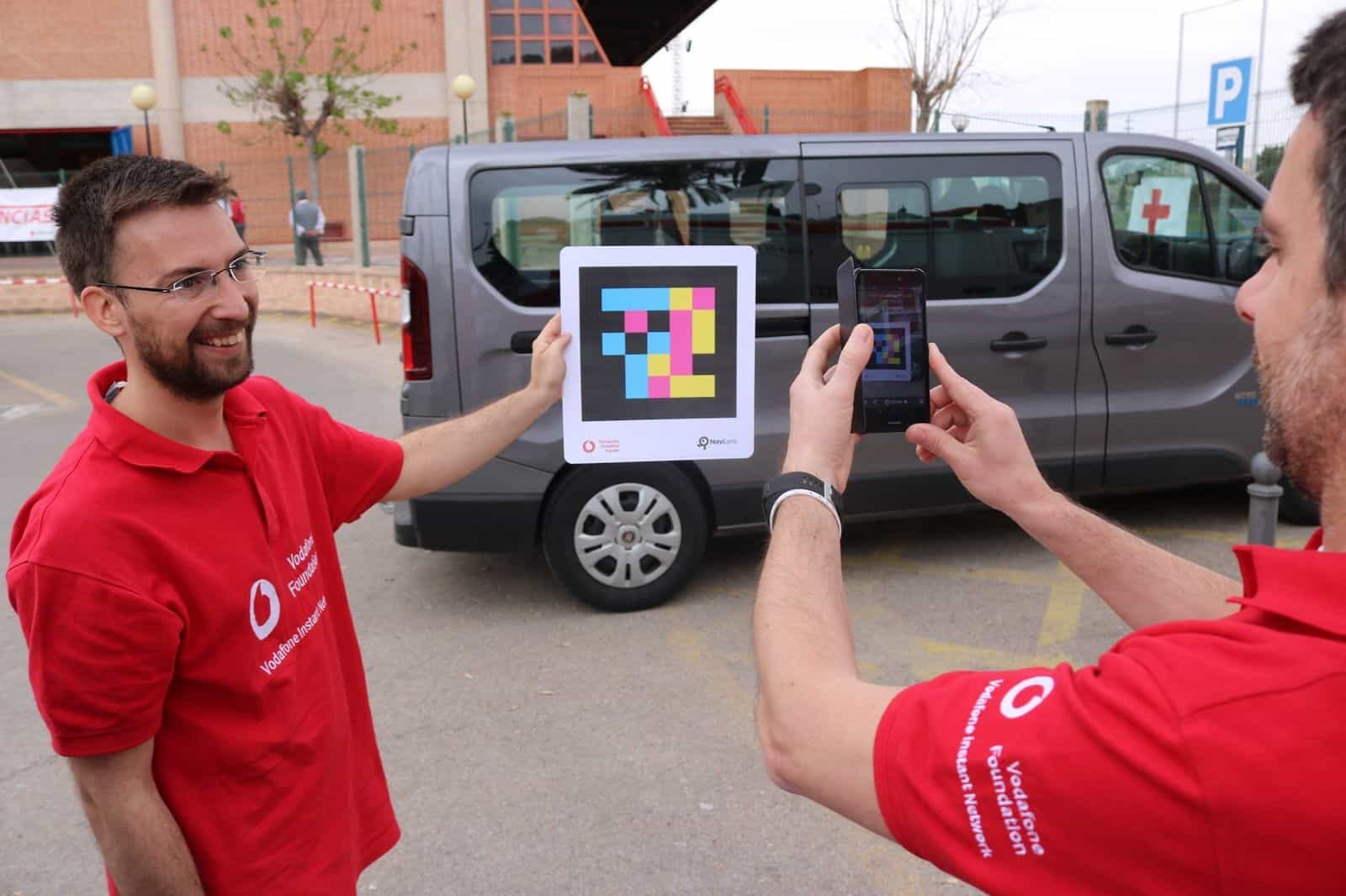Vodafone Foundation Instant Network volunteers hold a sign with a NaviLens code next to a Spanish Red Cross van at the UME Murcia 2018 drill