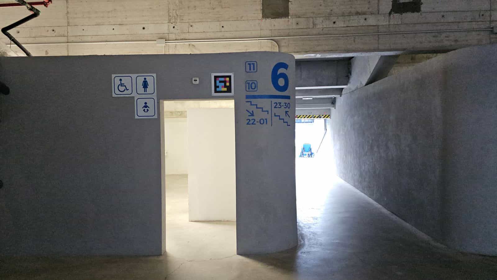 Umlauf im Reale Arena — NaviLens-Code an der Wand neben der Tür zum barrierefreien WC, mit Piktogrammen für Rollstuhl, Damen und Wickelraum sowie der blauen Beschilderung für Tribünen 10 und 11, Sektor 6 und Reihen 22-01 und 23-30