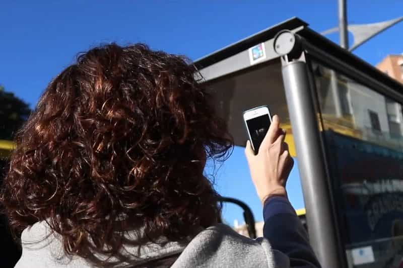 City bus stop in Murcia, Spain: a woman holds up her phone to scan the NaviLens code on the shelter roof