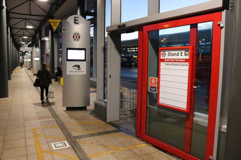 Stazione degli autobus di Wolverhampton: codici NaviLens sul pavimento, sulla colonna della banchina E e sul tabellone delle partenze, con una viaggiatrice che attraversa l’atrio